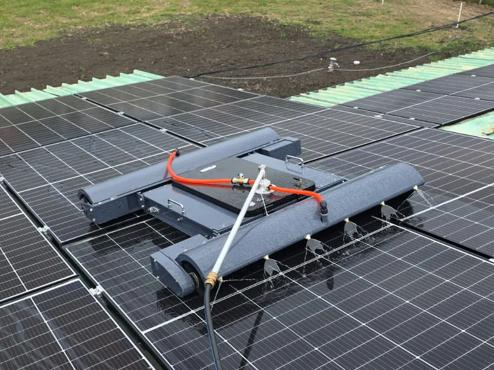 Robot DUO UnicleanSolar pe acoperișul unei hale, cu rânduri de panouri fotovoltaice și câmpul în fundal