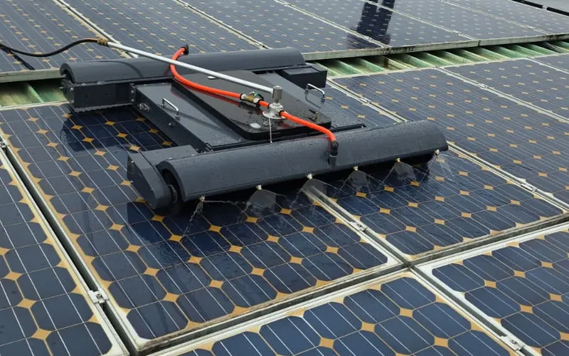 Robot DUO UnicleanSolar pe un acoperiș cu panouri, operatorul îl urmărește din spate