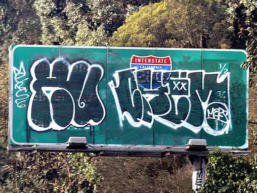 Panou rutier vandalizat cu graffiti, pe marginea unei autostrăzi